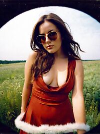 A 21 year old woman with short hair and a red dress lounges in a sunlit meadow